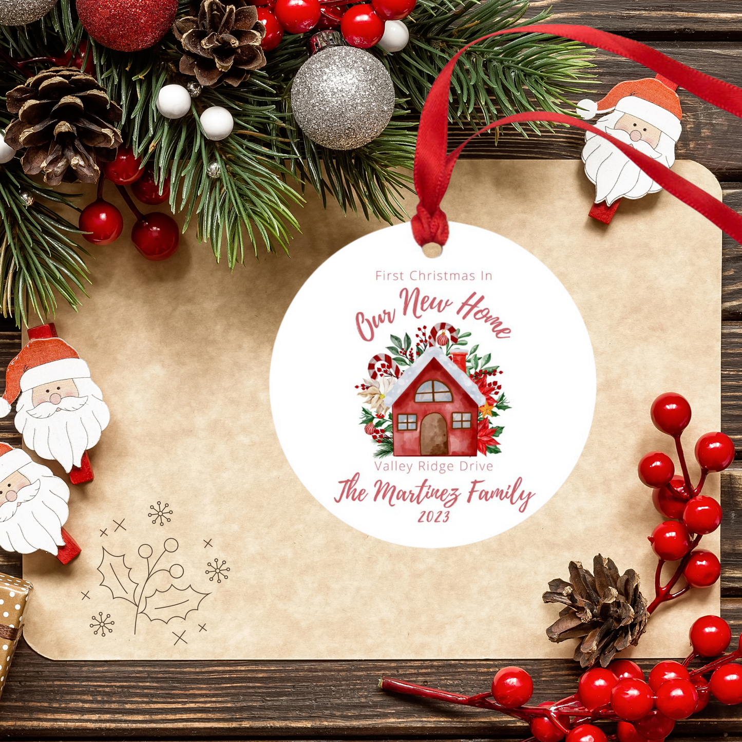 white ornament with a red ribbon has a cute red house with candy canes, greenery and red flowers behind it to depict a christmas image the words first christmas in our new home are above the house and valley ridge drive and the martinez family 2023 are under the house in a beautiful script font
