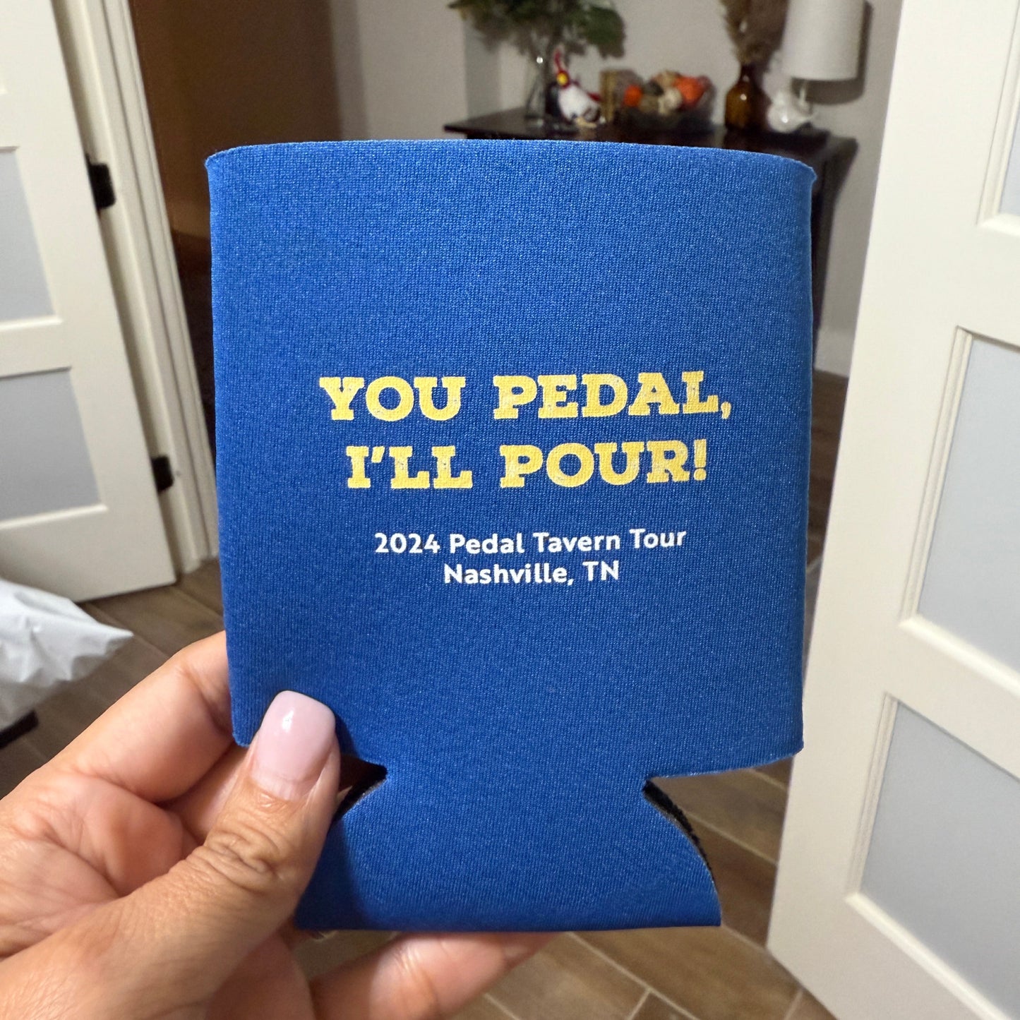 Blue can cooler with yellow text held in a hand, indoor setting
