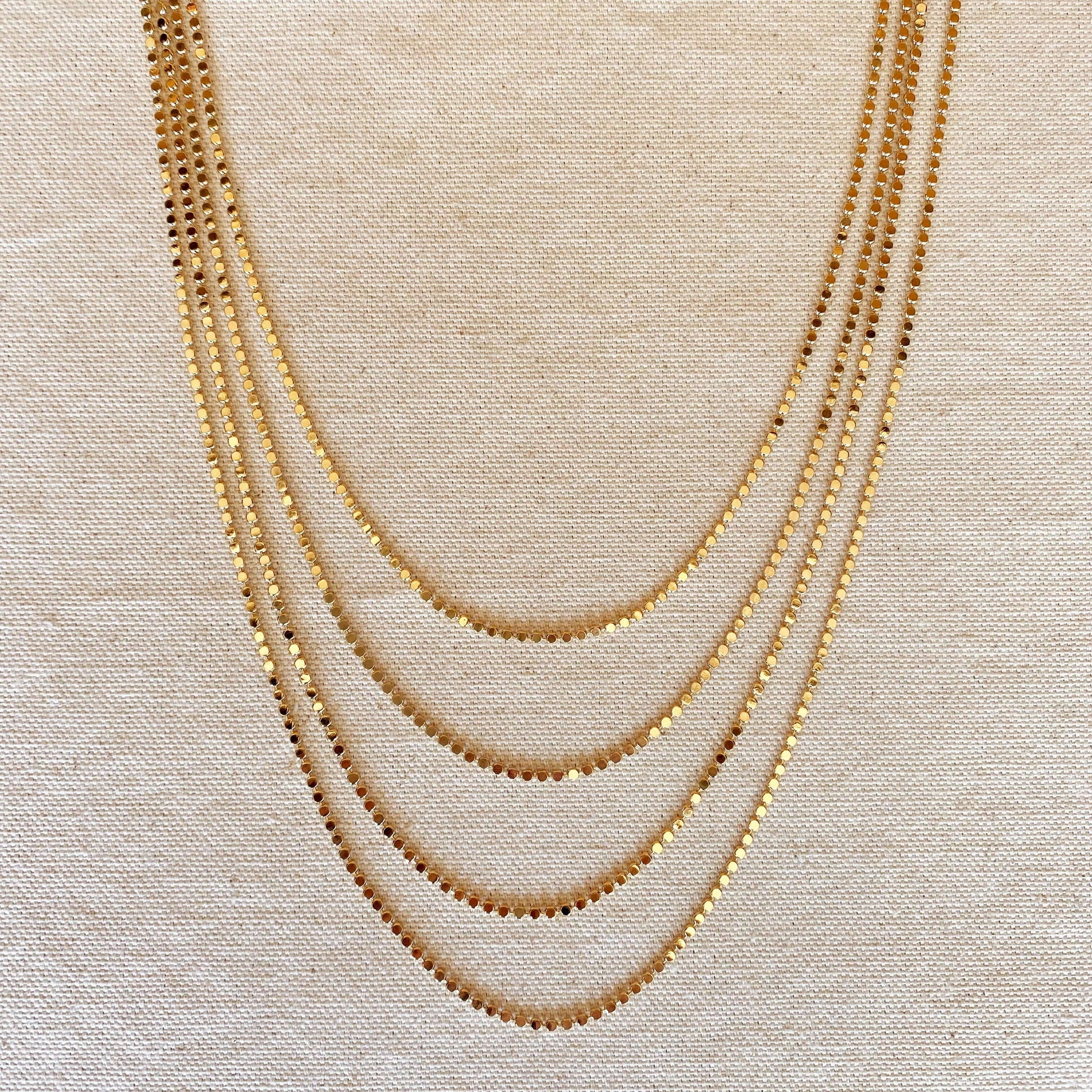 multiple layered tarnish free flat ball 18 karat gold filled necklaces laying flat on a canvas background
