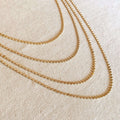 side view of multiple layered tarnish free flat ball 18 karat gold filled necklaces laying flat on a canvas background