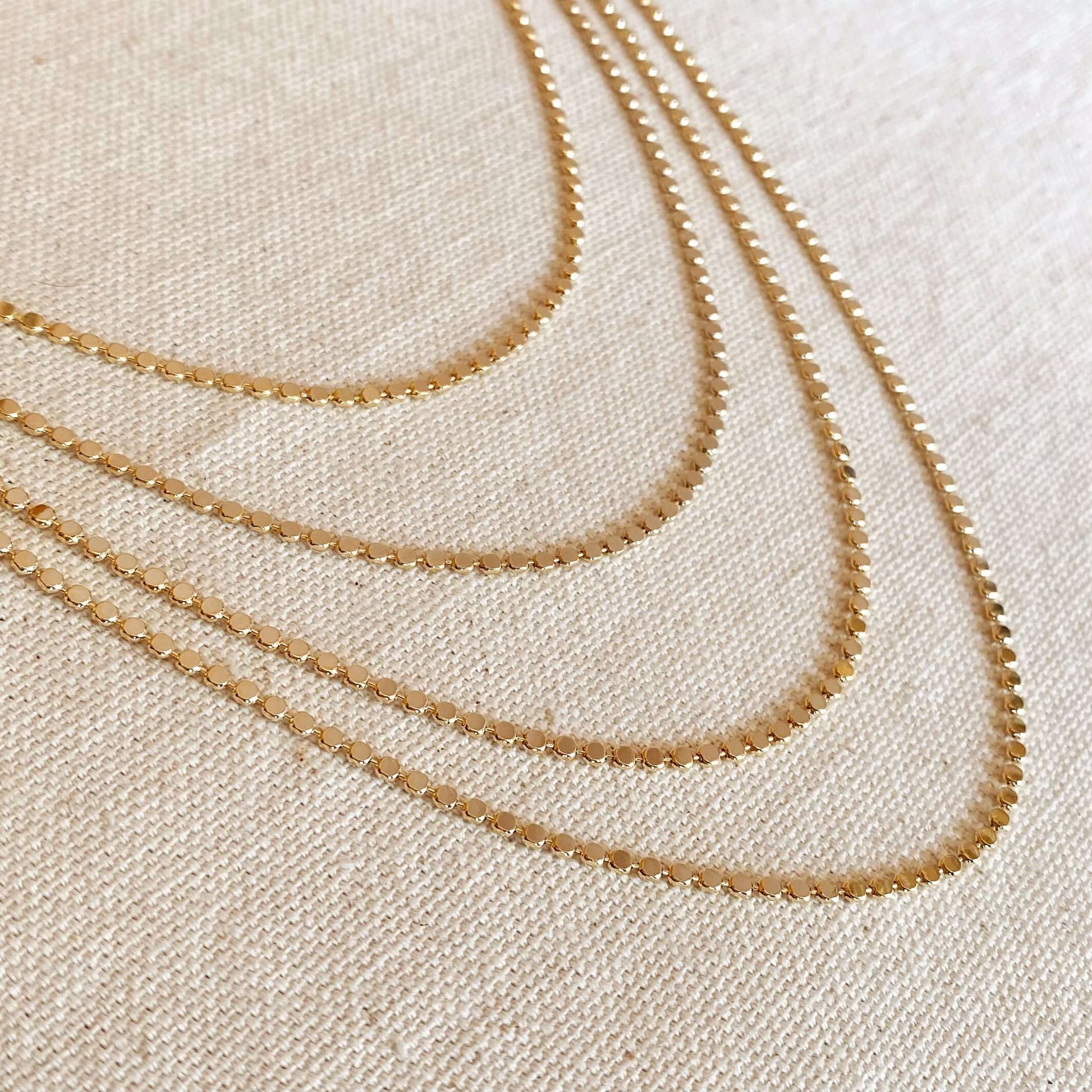side view of multiple layered tarnish free flat ball 18 karat gold filled necklaces laying flat on a canvas background
